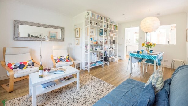 Ein Wohnzimmer mit Sofa, Couchtisch, Bücherregal und Essbereich mit Tisch und Stühlen.