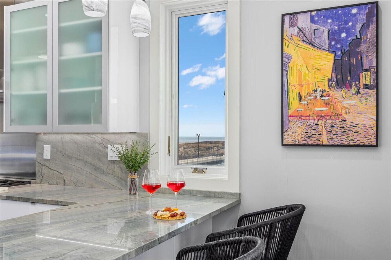 A modern kitchen with a marble countertop, two wine glasses, and a small plant.