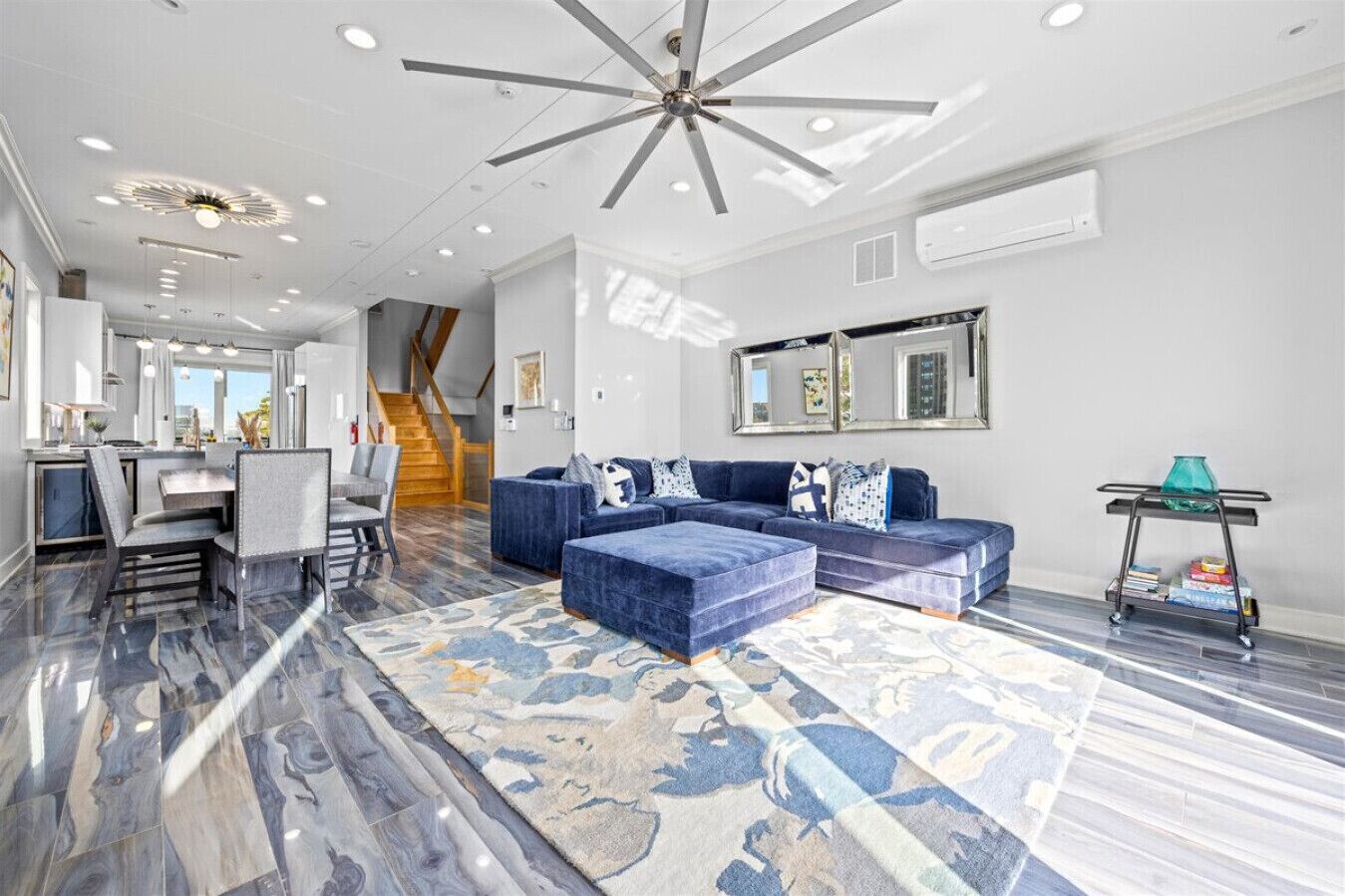 A modern living room with a sectional sofa, a dining area with a table and chairs, and a staircase leading to another level.