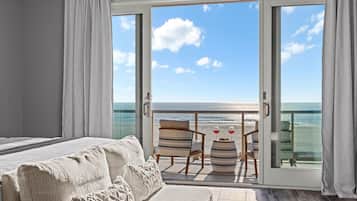 A bedroom with a large bed, a balcony with a table and chairs, and a view of the ocean.