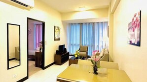 A hotel room with a dining area, a TV, a bed, and a view of the outside through curtains.