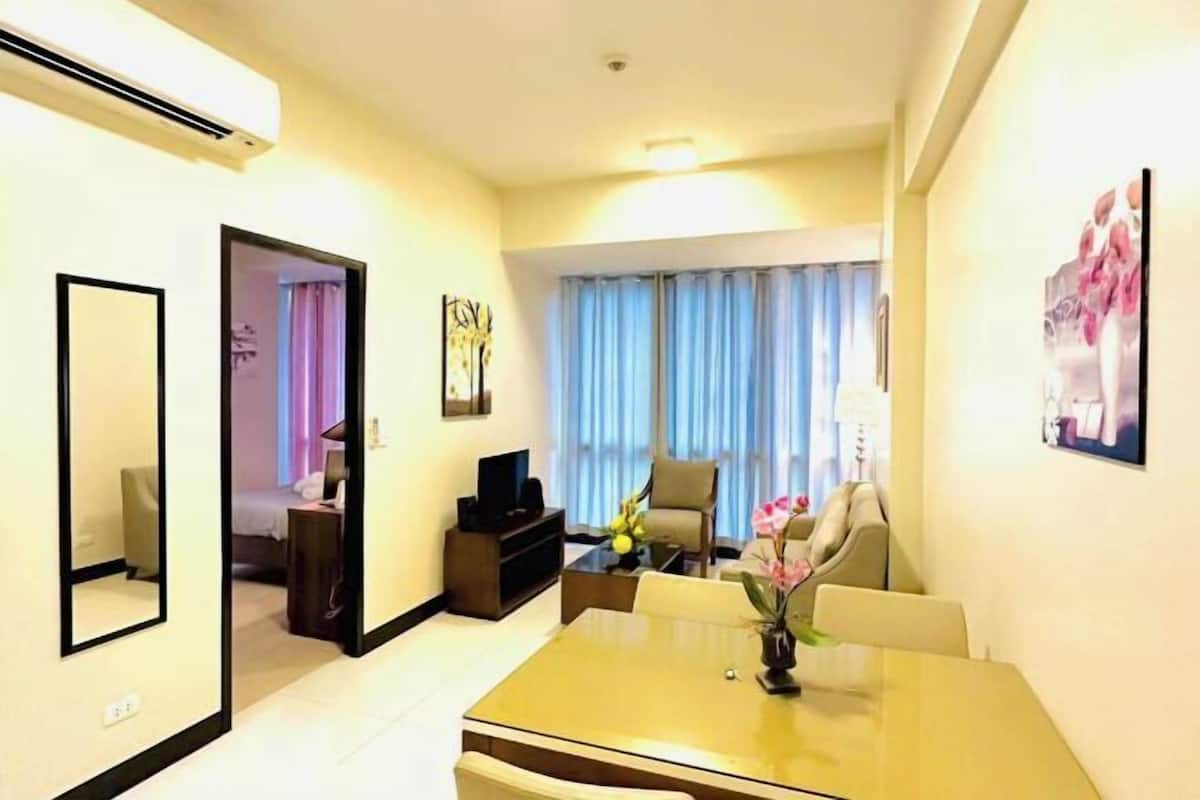 A hotel room with a dining area, a TV, a bed, and a view of the outside through curtains.