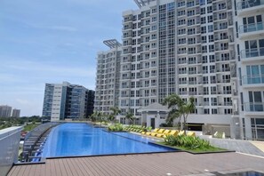 A swimming pool with a wooden deck, surrounded by a modern building with multiple floors and balconies. - One Pacific Place by Hiverooms (Lapu-Lapu City)