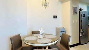 A dining area with a round table, four chairs, a decorative clock, and a refrigerator in the background.