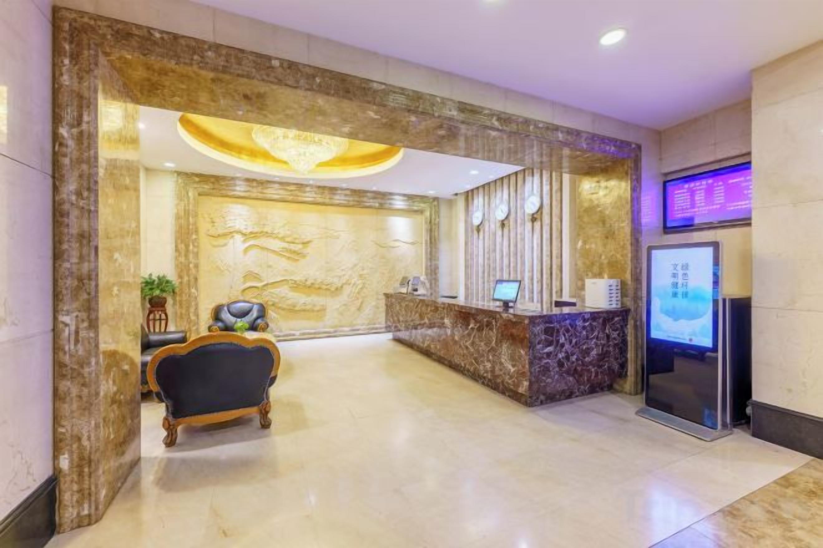 A hotel reception area with a marble reception desk, a seating area with a chair, and a digital information display.