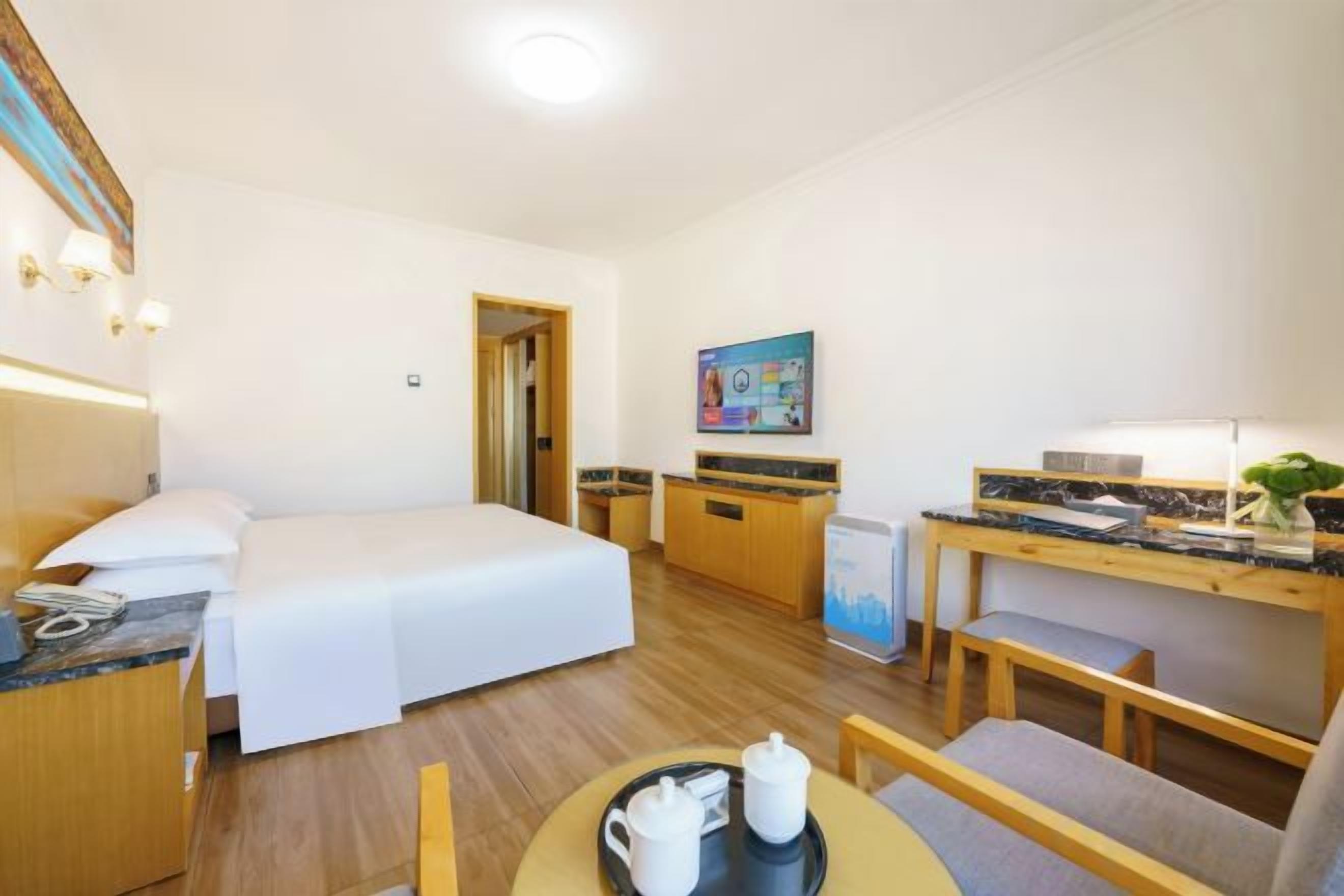 Habitación de hotel con cama, escritorio, silla, mesita con bandeja y televisor.