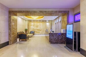 A reception area with a marble reception desk, a seating area with a sofa and chairs, and a wall-mounted digital display. - Friendly Hotel (Meimei Shopping Center Autonomous Region Museum Branch) (Urumqi)