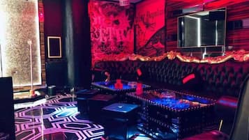 Uma área de bar com piso estampado, balcão e tela de televisão.