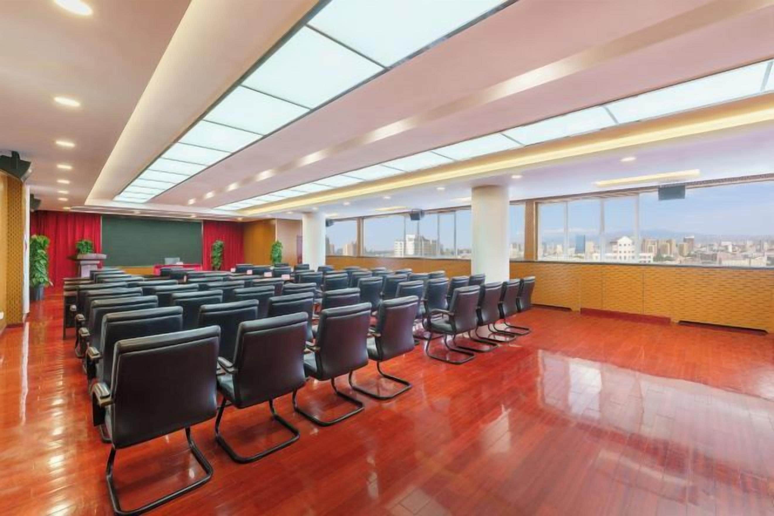 A conference room with rows of chairs, a stage, and large windows offering a city view.