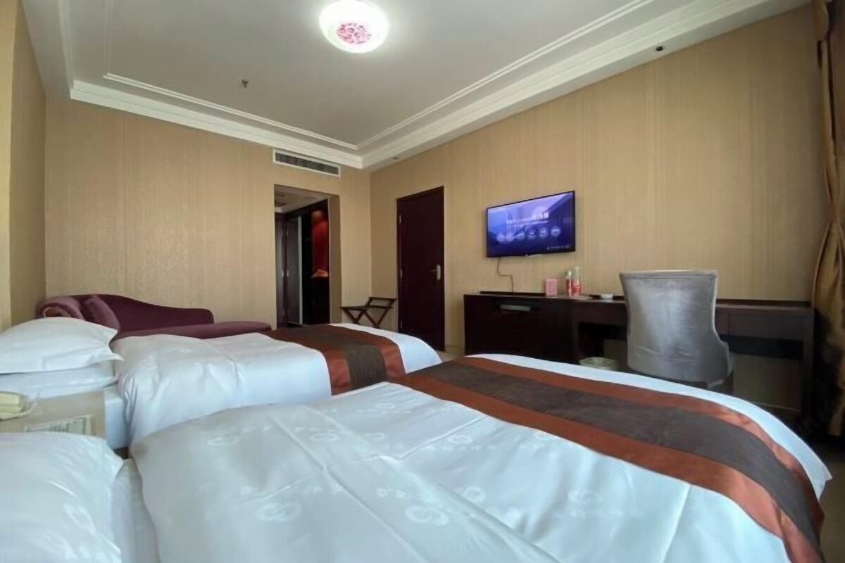 A hotel room with two beds, a television, a desk, and a chair.