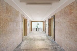 A hallway with marble walls and a concrete floor, leading to a room with a window and a table with a vase. - Friendly Hotel (Meimei Shopping Center Autonomous Region Museum Branch) (Urumqi)
