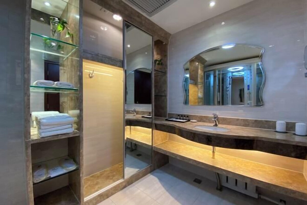 A modern bathroom with a glass shower enclosure, a large mirror, and a marble countertop.