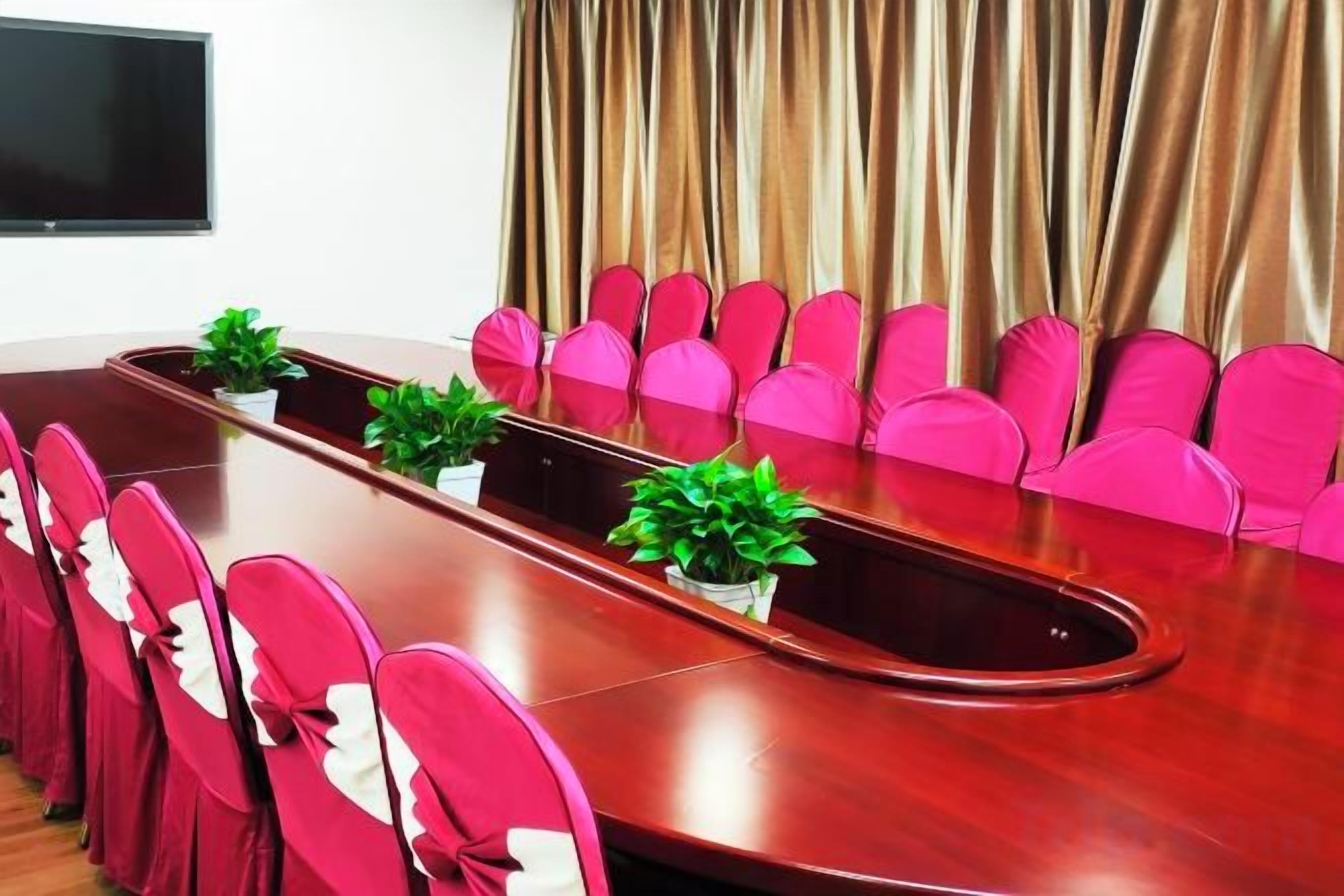 A conference room with a long table, pink chairs, and potted plants.