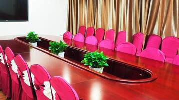 A conference room with a long table, pink chairs, and potted plants.