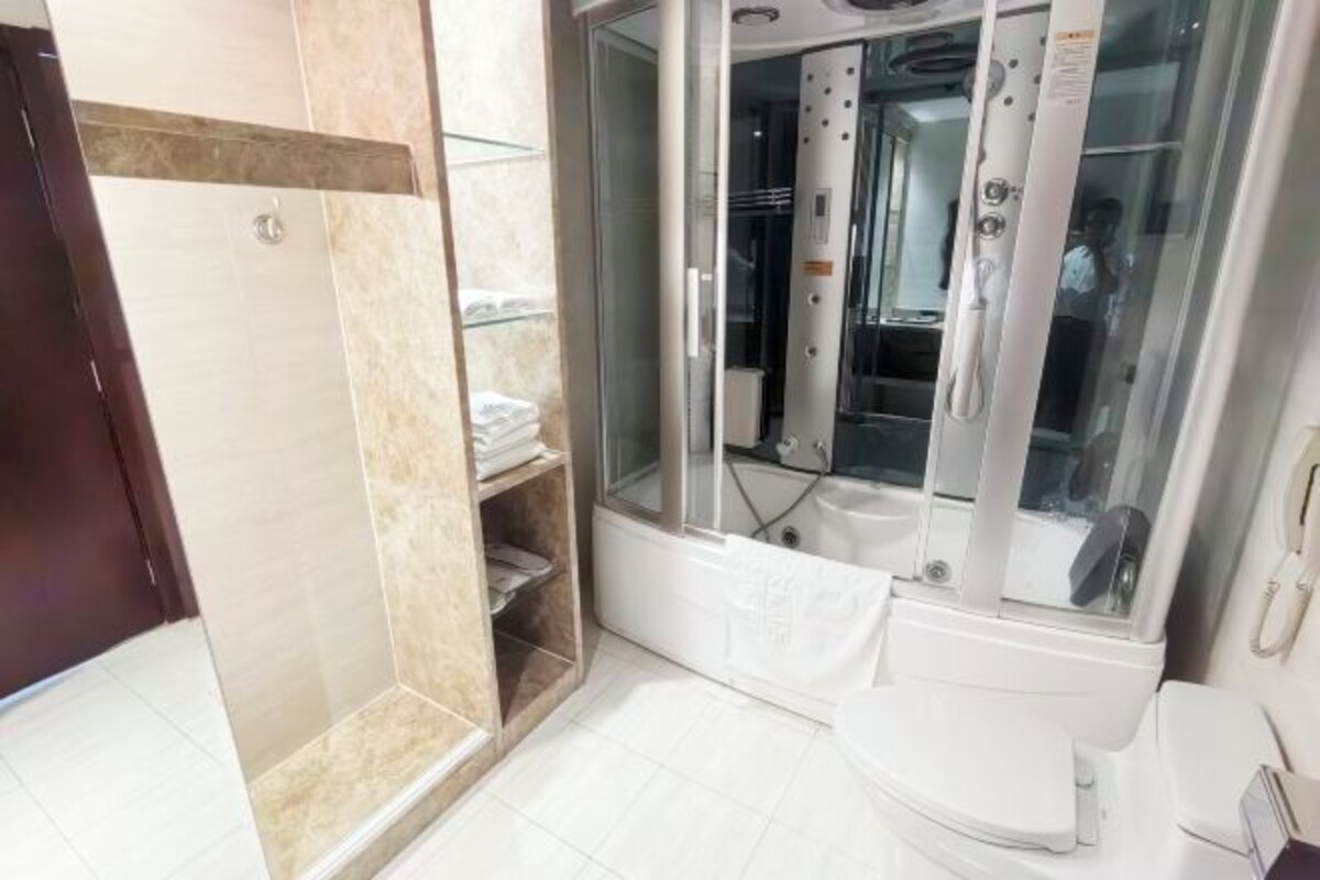 Une salle de bain avec une douche à parois de verre, des toilettes et une étagère avec des serviettes.