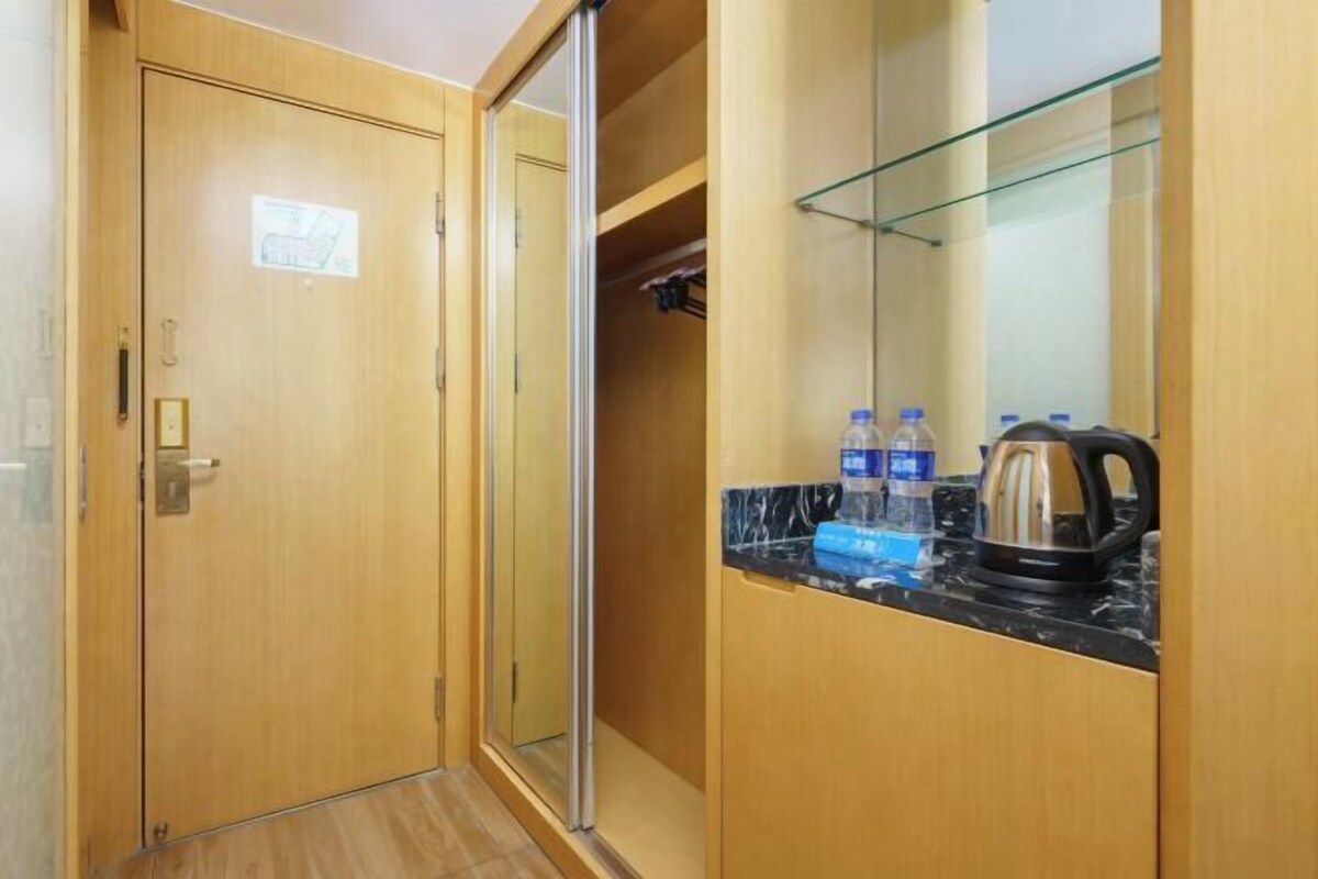 A hotel room with a wooden wardrobe, a glass shower enclosure, and a countertop with a kettle and water bottles.
