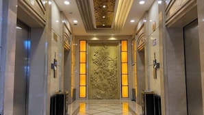 A hotel lobby with a marble floor, a central floral wall, and two elevators. - Friendly Hotel (Meimei Shopping Center Autonomous Region Museum Branch) (Urumqi)