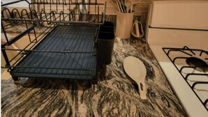 Une cuisine avec un étagère métallique noire, une cuillère blanche et une cuisinière.