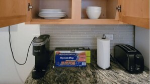 Une cuisine avec des meubles de rangement en bois, un plan de travail avec une machine à café, une boîte de papier d’aluminium de la marque Reynolds Wrap, un distributeur d’essuie-tout et un grille-pain.