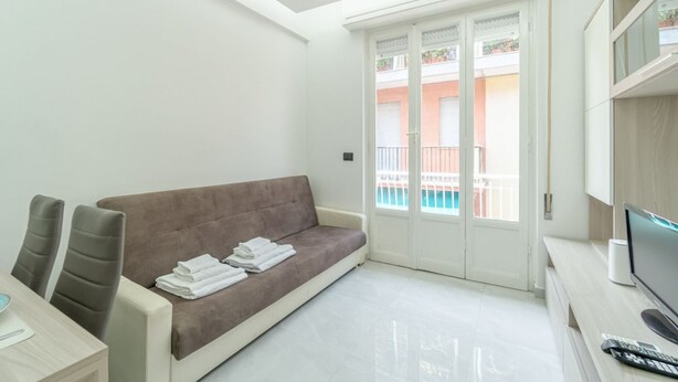 Un salon moderne avec un canapé, un téléviseur et un balcon offrant une vue sur les immebles.