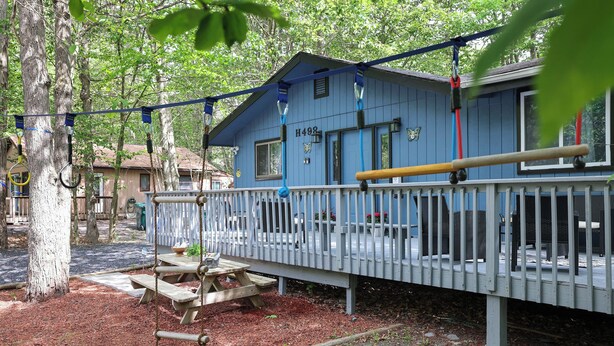 A blue building with a number 'H498' on the side, a wooden deck, and a swing set. - Fun Home w/AC and TVs  In All/Pool Nearby/BBQ Grill/Firpit/Games/Amenities/
 (Tobyhanna)