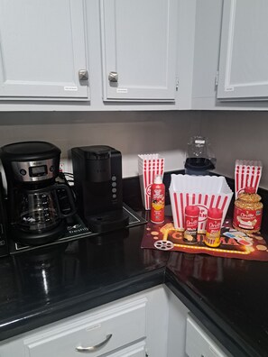 A kitchen counter with a coffee maker, a toaster, popcorn containers, and a popcorn container with a label.