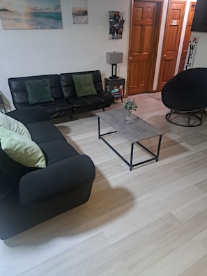 Un salon avec un canapé noir, une table basse, un fauteuil noir et une porte en bois.