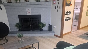 A living room with a fireplace, a sofa, a coffee table, and a door leading to a kitchen. - Fun Home w/AC and TVs  In All/Pool Nearby/BBQ Grill/Firpit/Games/Amenities/
 (Tobyhanna)