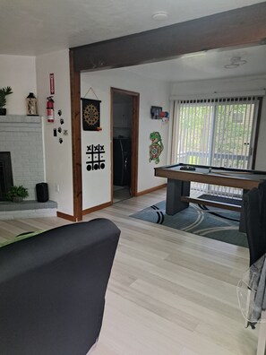 A living room with a pool table, a dartboard, and a fireplace.