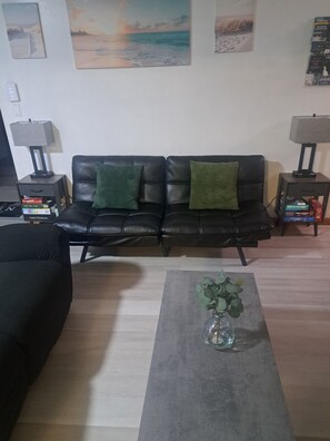 Ein Wohnzimmer mit einem schwarzen Ledersofa, zwei grünen Kissen, einem Couchtisch mit einer Vase und einer Wand mit gerahmten Bildern.