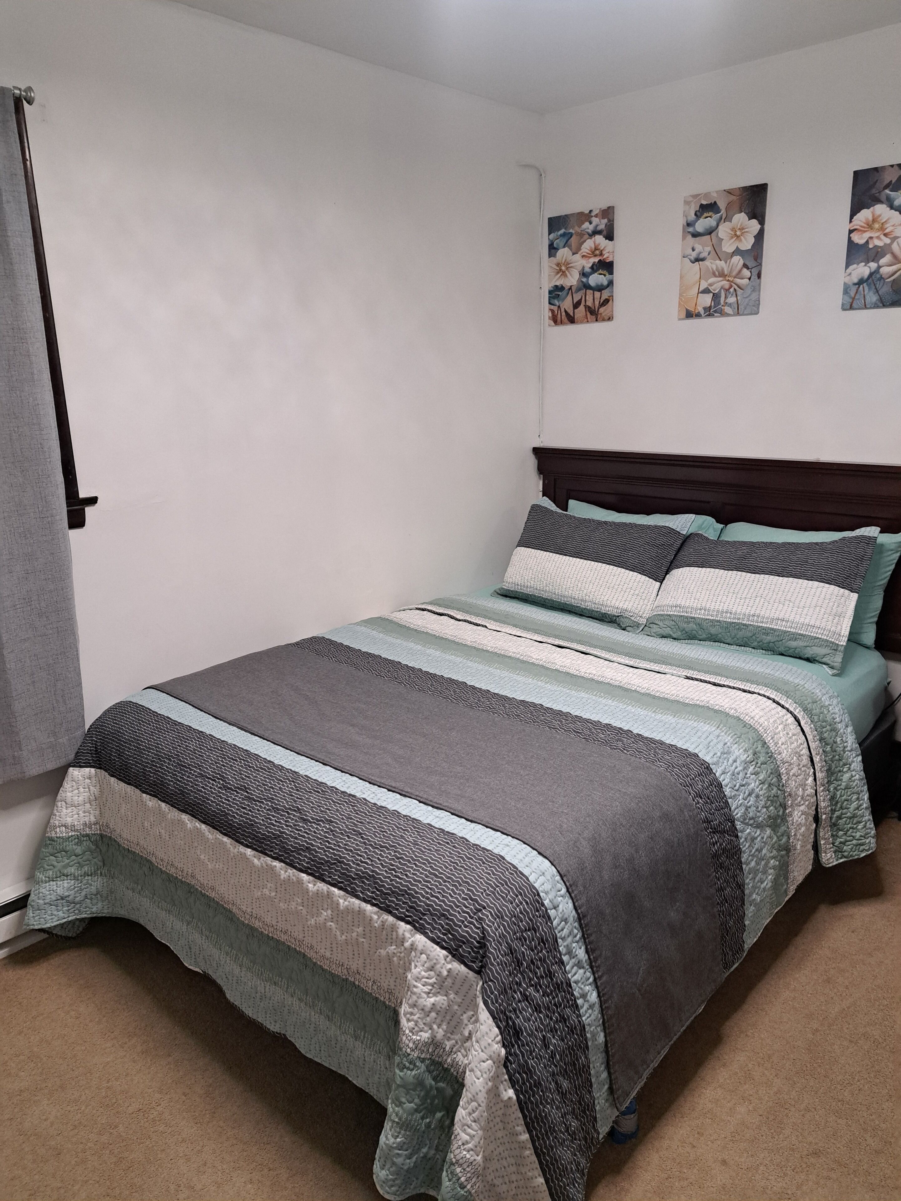 A bedroom with a bed, a headboard, and three wall-mounted floral paintings.