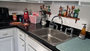 A modern kitchen with white cabinets, a black countertop, and stainless steel appliances. There are various kitchen items and utensils on the shelves and countertop. - Fun Home w/AC and TVs  In All/Pool Nearby/BBQ Grill/Firpit/Games/Amenities/
 (Tobyhanna)