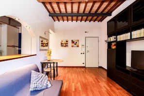 A modern interior with a wooden ceiling, a sofa with a patterned pillow, a small round table with a vase, and a bookshelf with books and decorative items.