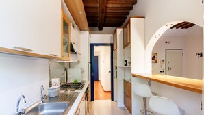 Una cocina estrecha con lavamanos de acero inoxidable, estufa y armarios blancos.