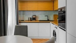 A compact kitchen with white cabinets, a wooden countertop, a washing machine, and a dining area with a round table and two chairs. - Lozenets apartment (Sofia)