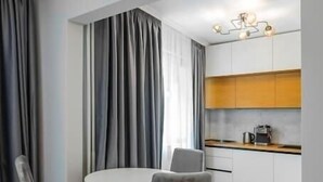 A modern dining area with a round table and four chairs, a kitchen with white cabinets and a wooden countertop, and a herringbone-patterned wooden floor. - Lozenets apartment (Sofia)