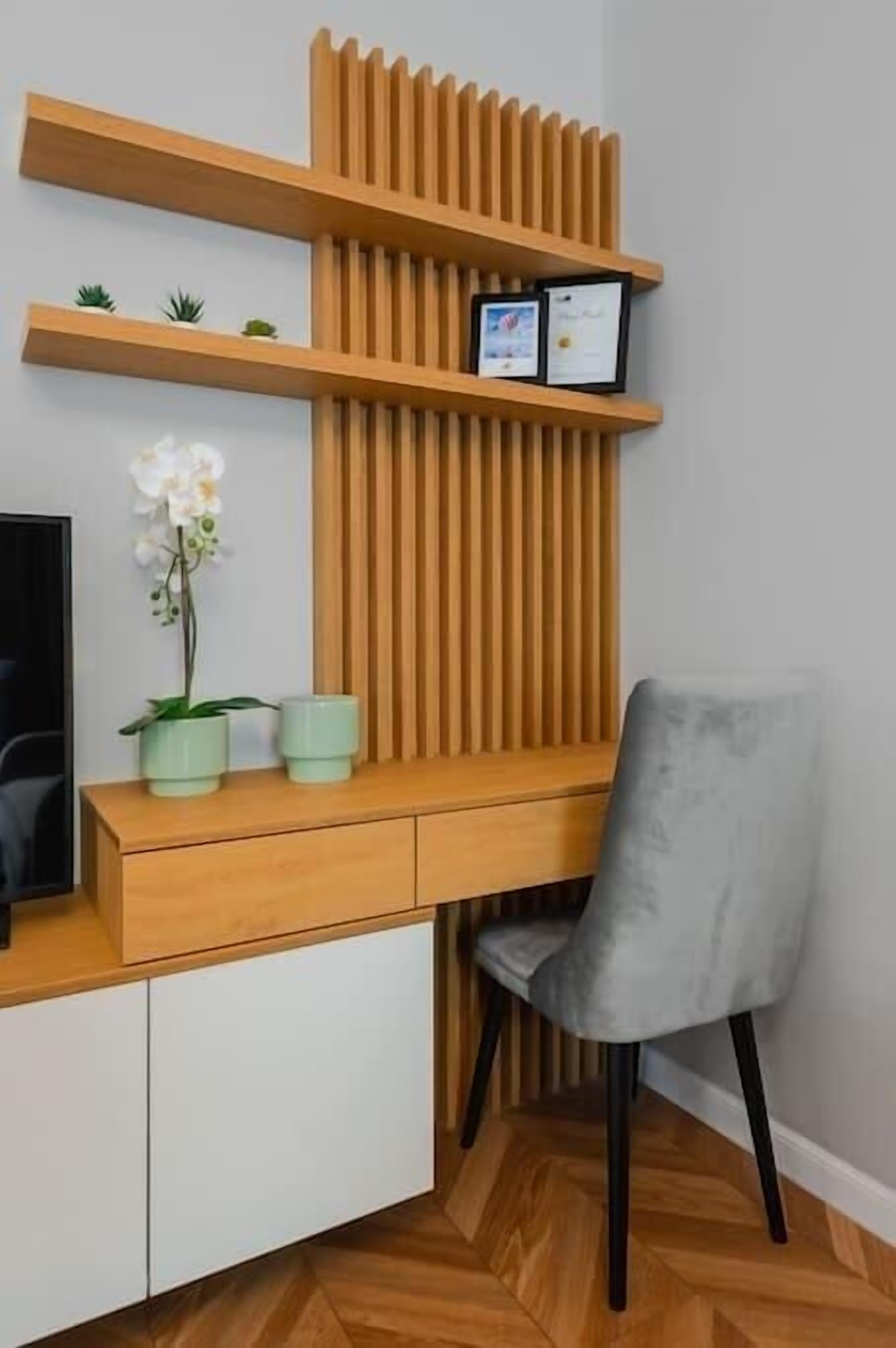 Un escritorio moderno con diseño de listones de madera, una silla gris y una pequeña orquídea en maceta.
