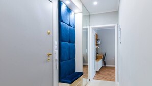 A hallway with a blue cushioned bench, a wooden floor, and a door leading to a room with a desk and chair. - Lozenets apartment (Sofia)