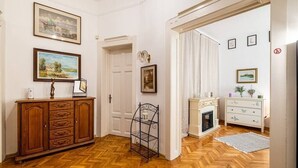 Une pièce dotée d’un parquet en bois disposé en motif à chevrons, d’un meuble en bois avec des tiroirs, d’une étagère en métal, d’une cheminée et d’une commode blanche agrémentée d’objets décoratifs.