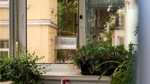 Une fenêtre donnant sur un immeuble, avec un pot de fleurs posé sur le rebord.