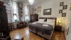 Une chambre à coucher avec un grand lit, un plancher en bois, des rideaux, un lustre et des tableaux encadrés accrochés au mur.