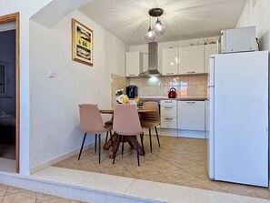Une cuisine compacte avec des meubles blancs, un réfrigérateur, une table à manger avec des chaises et un luminaire suspendu.