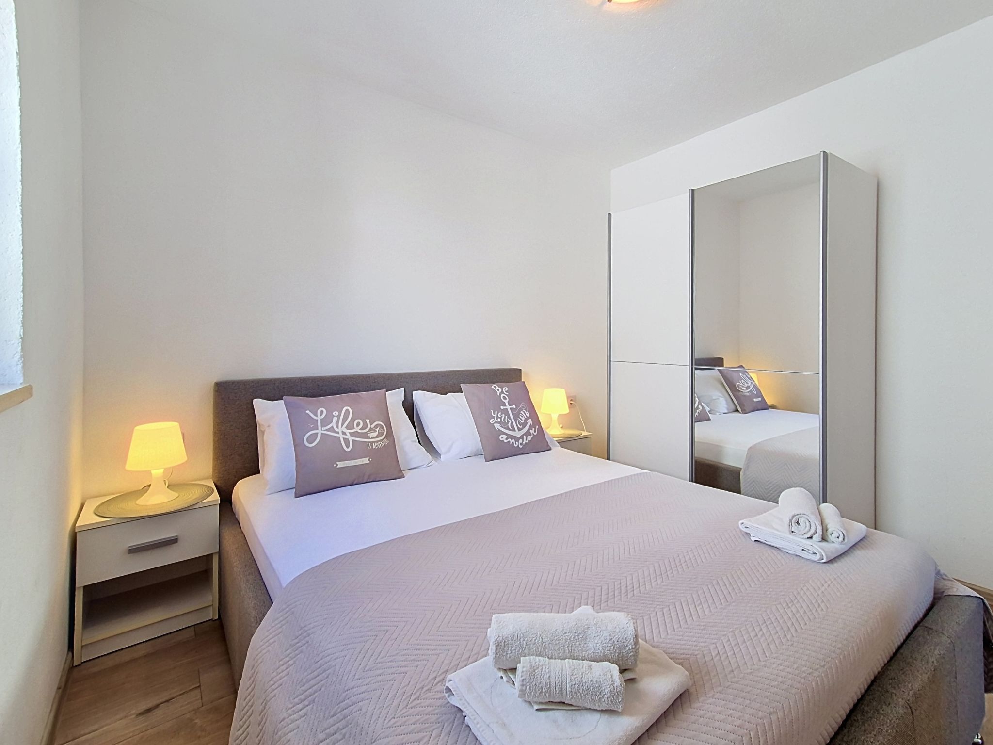 A hotel room with a bed, a nightstand with a lamp, a mirror, and towels on the bed.