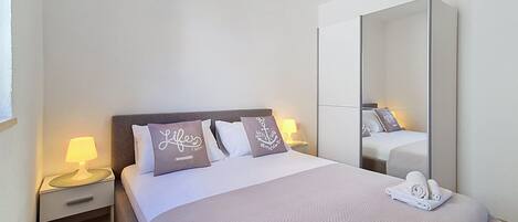 A hotel room with a bed, a nightstand with a lamp, a mirror, and towels on the bed.