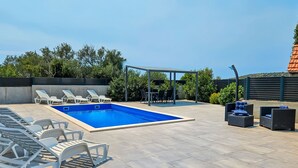 Una piscina con sillas de descanso y una zona de estar techada.