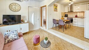 Una sala de estar moderna con un sofá, un televisor, un reposapiés rosa y un comedor con sillas y una mesa.