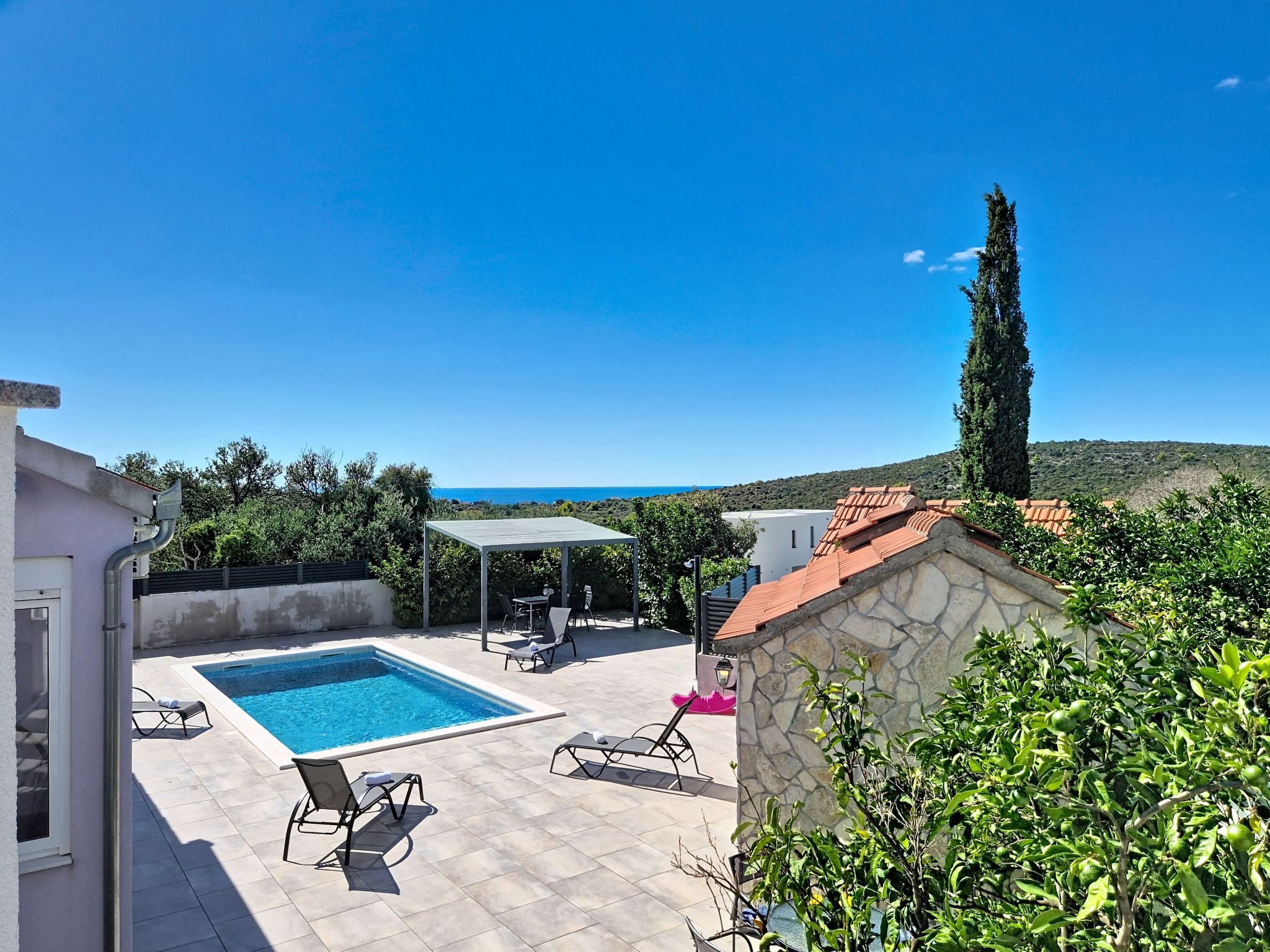 A swimming pool with lounge chairs, a pergola, and a stone wall.