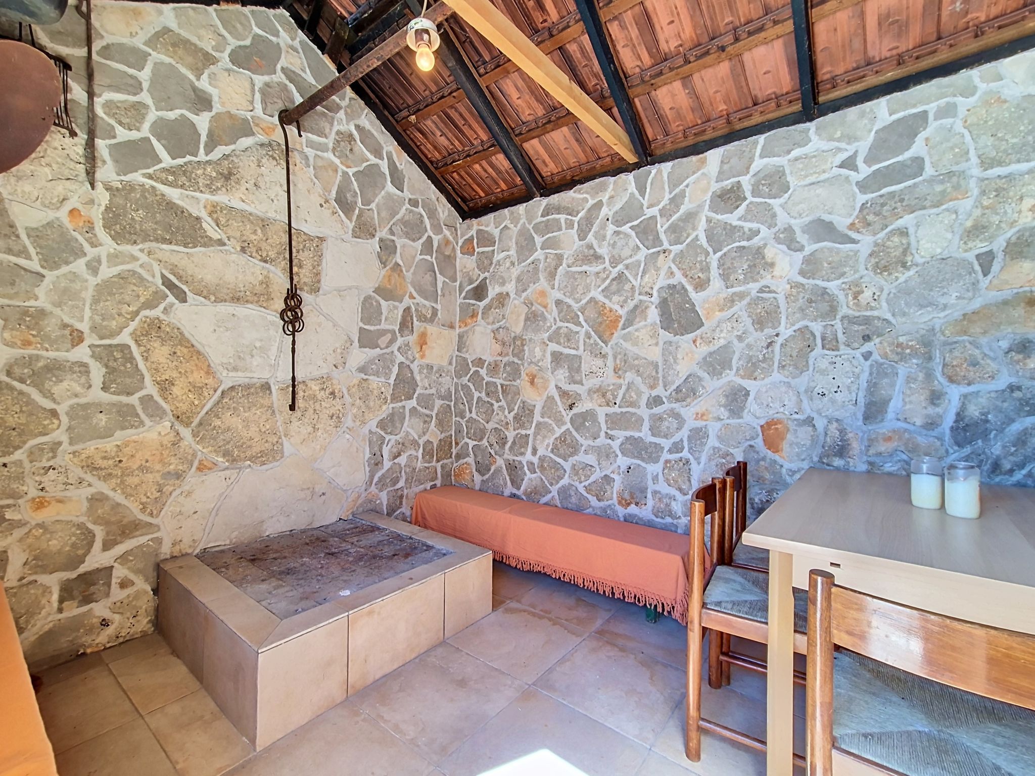 A stone-walled room with a wooden bench, a table, and a hanging light fixture.