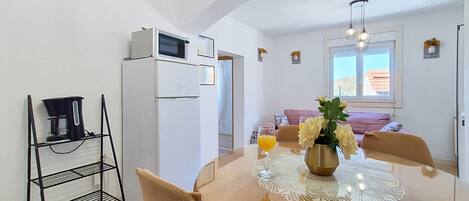 A modern kitchen with a dining table, chairs, a coffee machine, and a refrigerator.