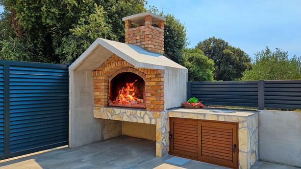 Un horno de ladrillo al aire libre con chimenea, base de piedra y puerta de madera.